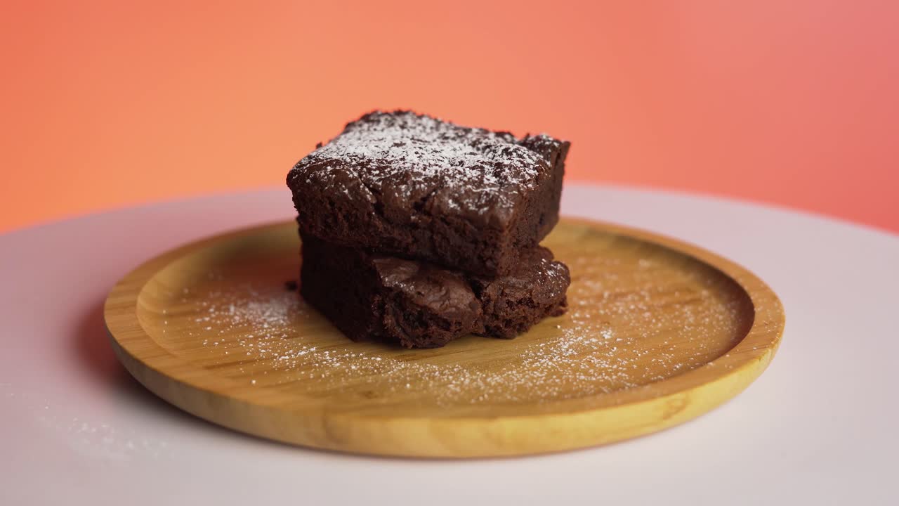 imágenes de 4k de delicioso brownie de chocolate con capa de azúcar girando en un plato de madera