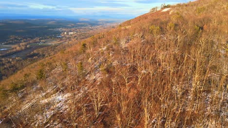 Aerial-footage-of-a-forested-mountain-valley-with-a-light-coating-of-snow-during-winter-in-the-Appalachian-Mountains-during-sunset’s-golden-hour-in-winter