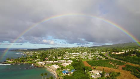 aerial pullback away from vibrant rainbow above golden green buildings, mountain, and ocean