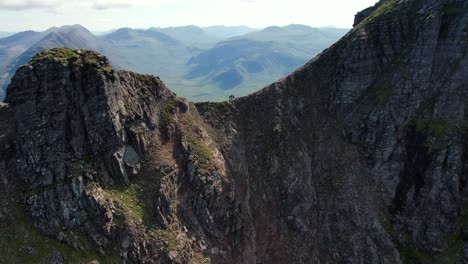 Three-people-walking-over-the-beautiful-stone-cliff-on-An-Teallach-in-the-United-Kingdom-on-a-cloudy-day