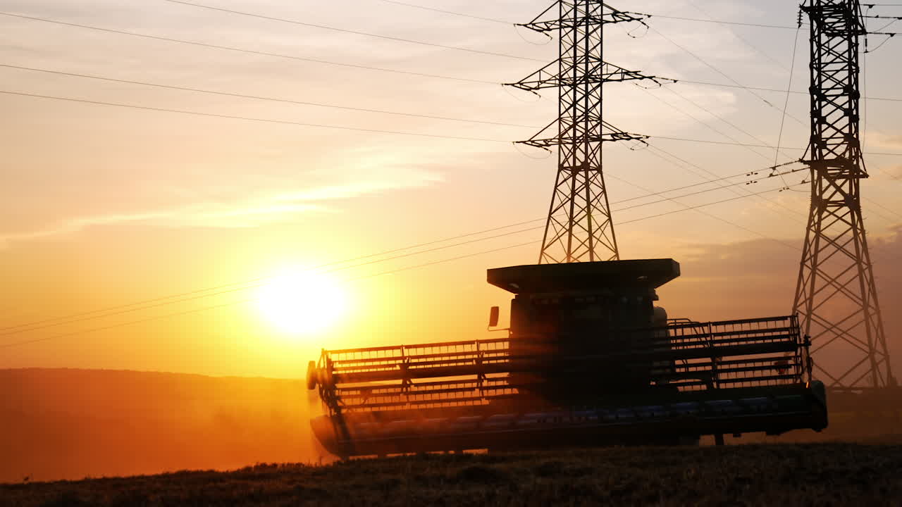 Harvesting at sunset in rural fields. A combine harvester works through fields as the sun sets, creating a beautiful silhouette against the vibrant sky