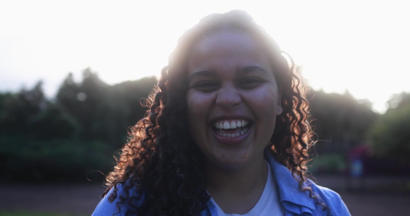 Jovem Mulher Feliz de Cabelo Cacheado Rindo ao Ar Livre sob a Luz do Sol