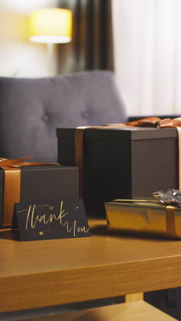 vertical video of man putting thank you card next to presents in gift wrapped boxes decorated with ribbon on table in lounge