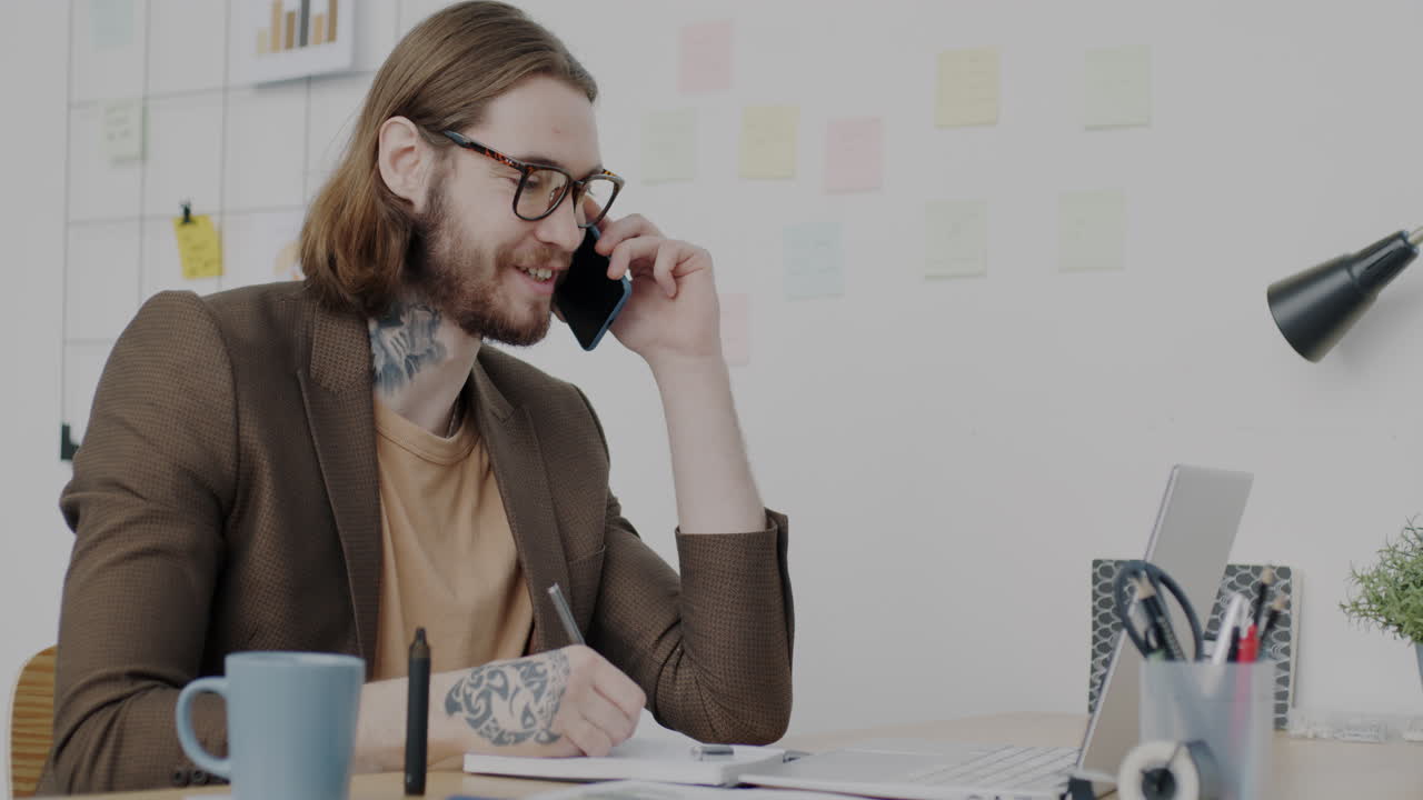 Man Working on Laptop and Talking on Phone in Office