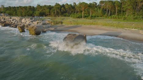 beautiful aerial establishing view of karosta concrete coast fortification ruins, sunny summer evening, golden hour light, stormy waves at baltic sea, slow motion drone orbit shot