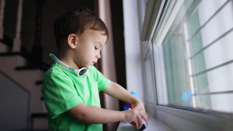cute toddler with plump cheeks stands at the window holding a toy. lovely baby boy playing with a car. blurred backdrop.