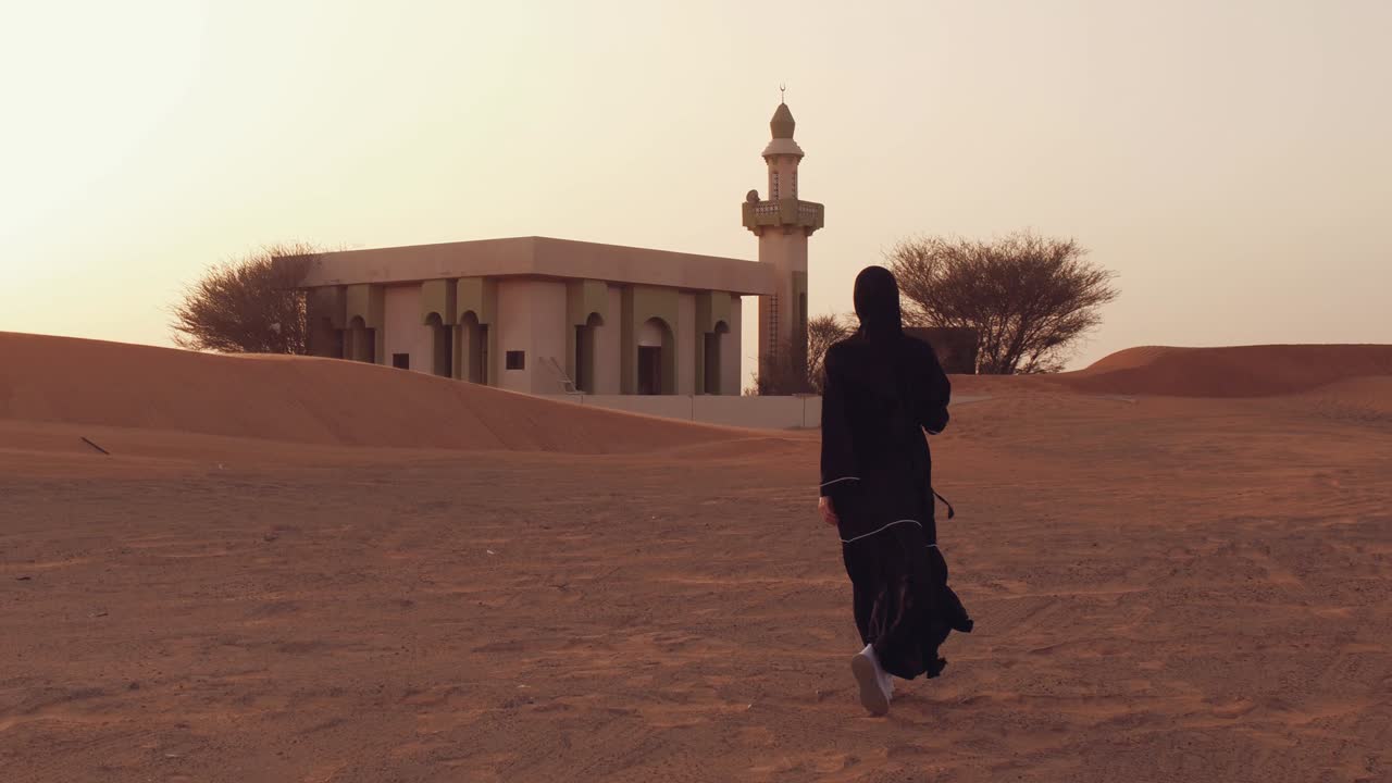 mujer musulmana de pie cerca de la mezquita en el desierto. viento fuerte oriente medio paz sin guerra