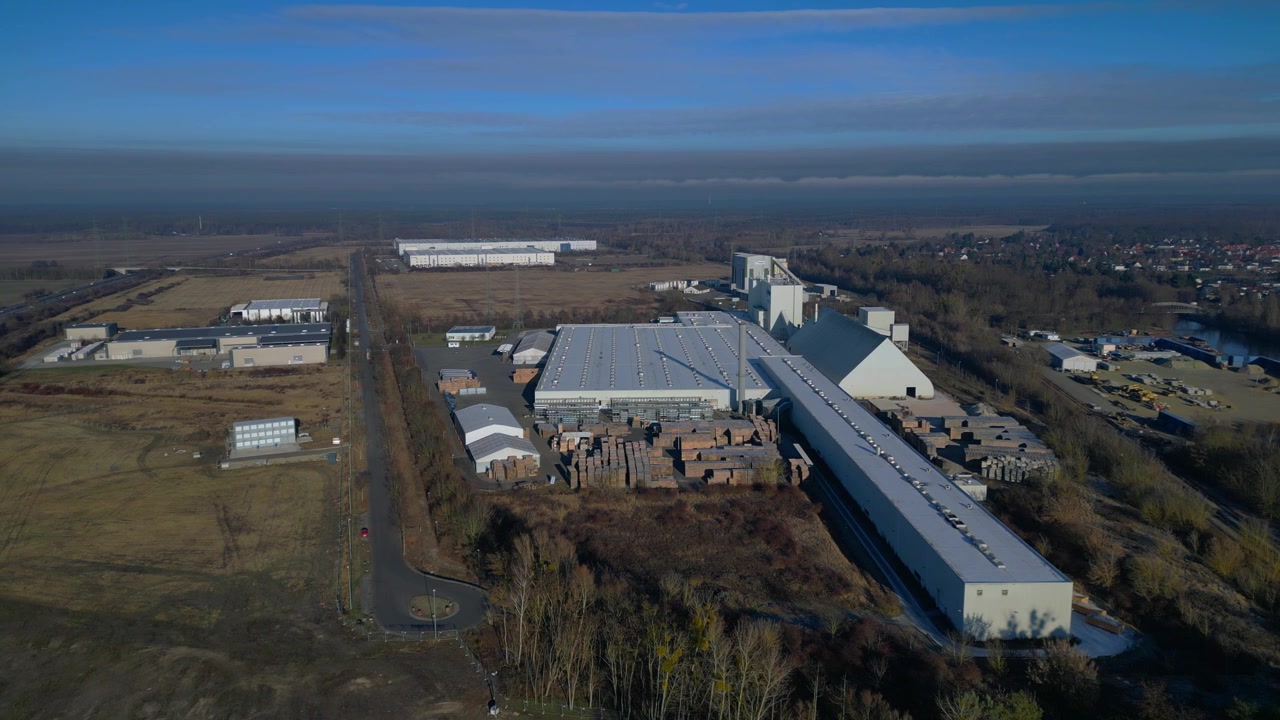 Large industrial complex featuring multiple factory buildings, material stockpiles, and silos against a clear sky. Stunning aerial view static panorama hovering drone