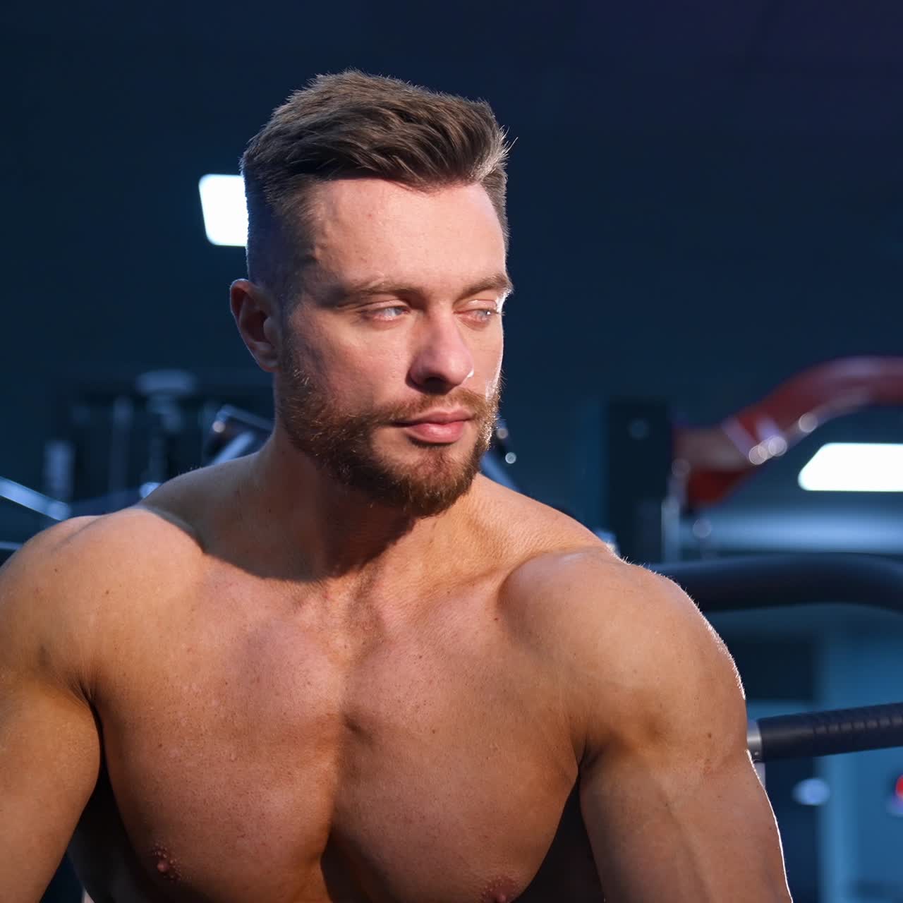 Man with perfect body train muscles on sport equipment and drinks water. View from the side on handsome man with perfect body