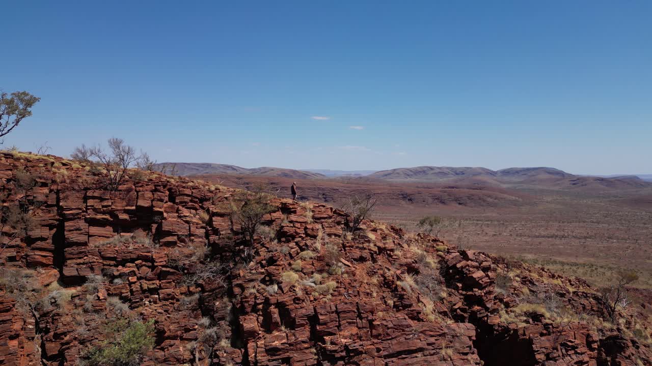 hombre caminando en el borde de las montañas rojas durante un día soleado en el desierto de australia - vista aérea