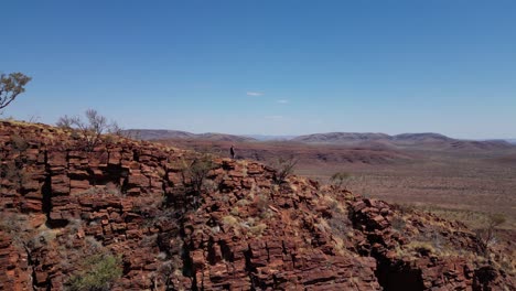 walking man on the edge of red mountains during sunny day in australia desert - aerial view