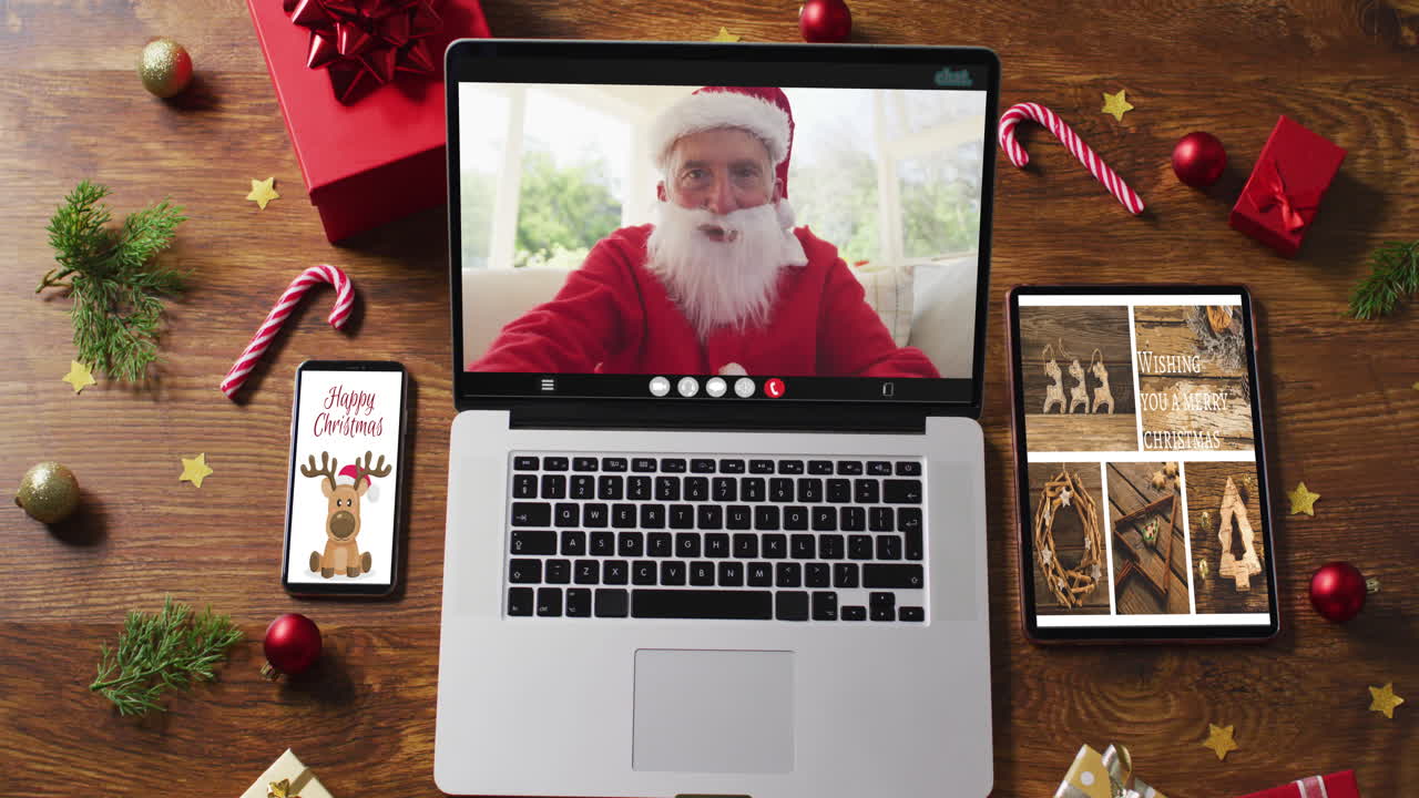 feliz senior caucásico santa en videollamada en computadora portátil, con teléfono inteligente, tableta decoraciones de navidad