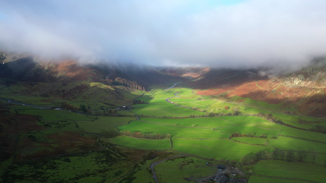 un amplio valle verde rodeado de nubes, montañas envueltas iluminadas por el sol de otoño de la mañana temprano.