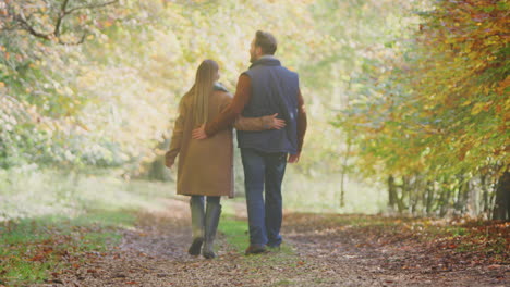 rear view of loving mature couple walking along track in autumn countryside