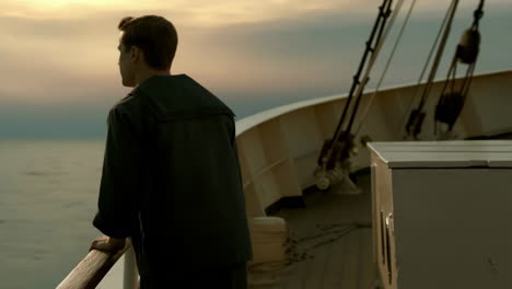 man in sailor uniform on ship deck looking at the ocean at sunset