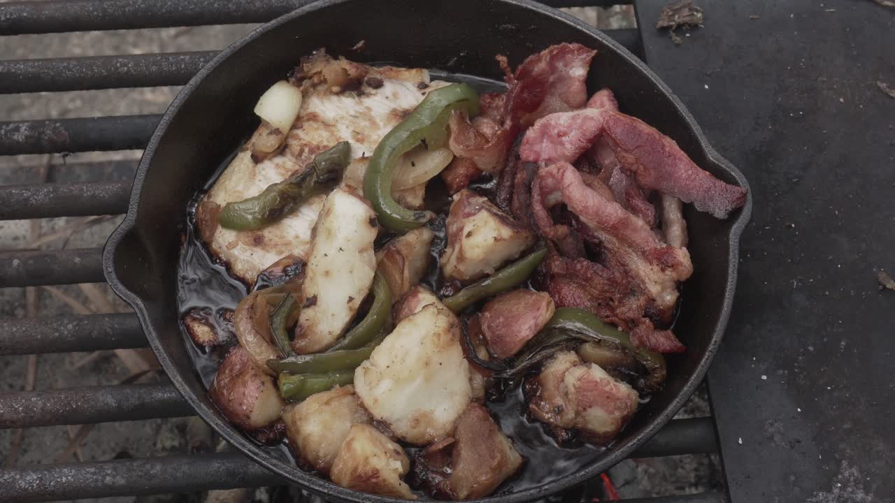 bacon, potatoes, green peppers, onions cooking in a cast iron skillet outdoors at a campground in 4k 29.97p