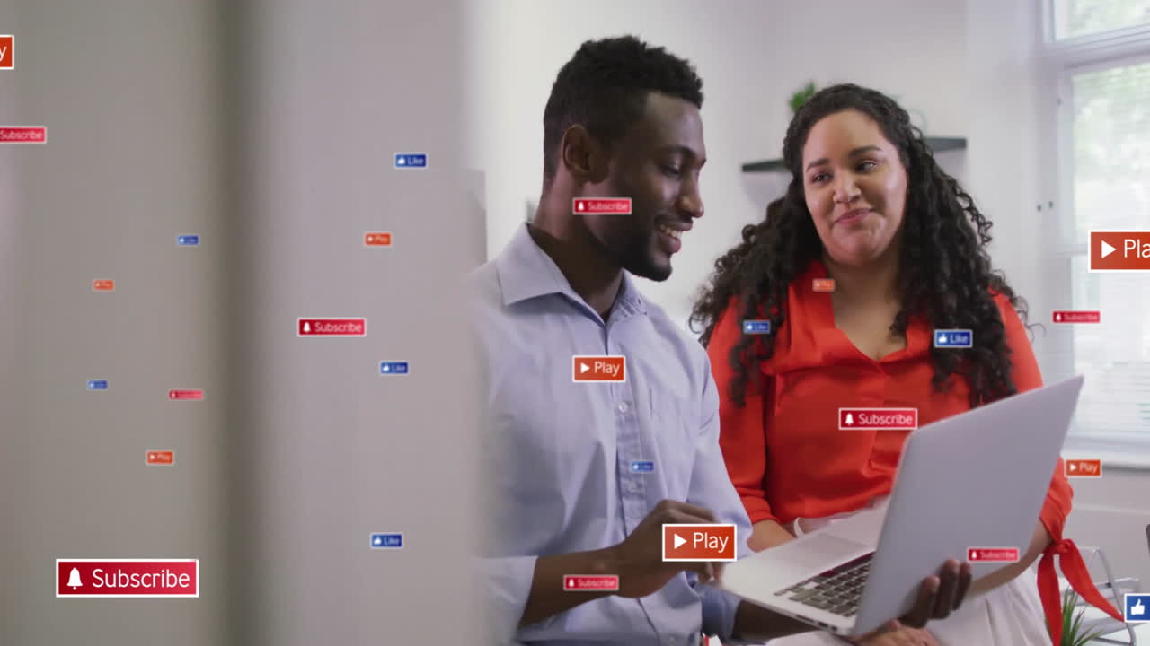 Two coworkers using laptop in tech office showing floating subscribe like play icons