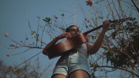 low shot of a indian girl playing the guitar under a tree