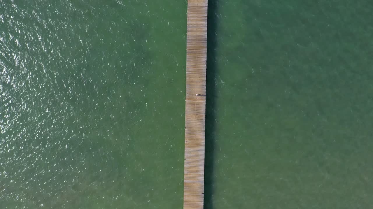 Veduta aerea dall'alto di turisti che camminano su un molo da pesca in legno con acque verde smeraldo, El Muellecito, Monte Cristi, Repubblica Dominicana