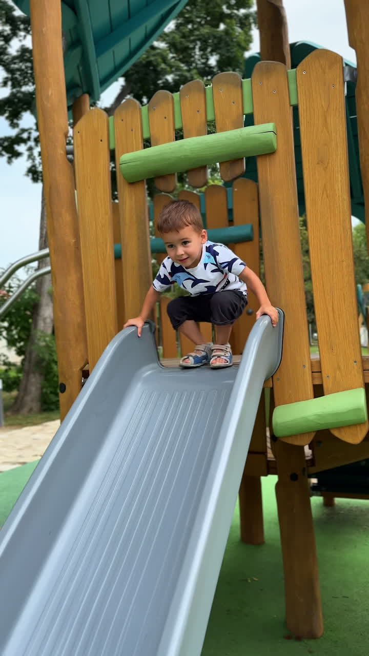 Lovely Caucasian baby is inside the wooden playhouse looking out of window. Kid moves to the slide and goes down quickly. Vertical video.