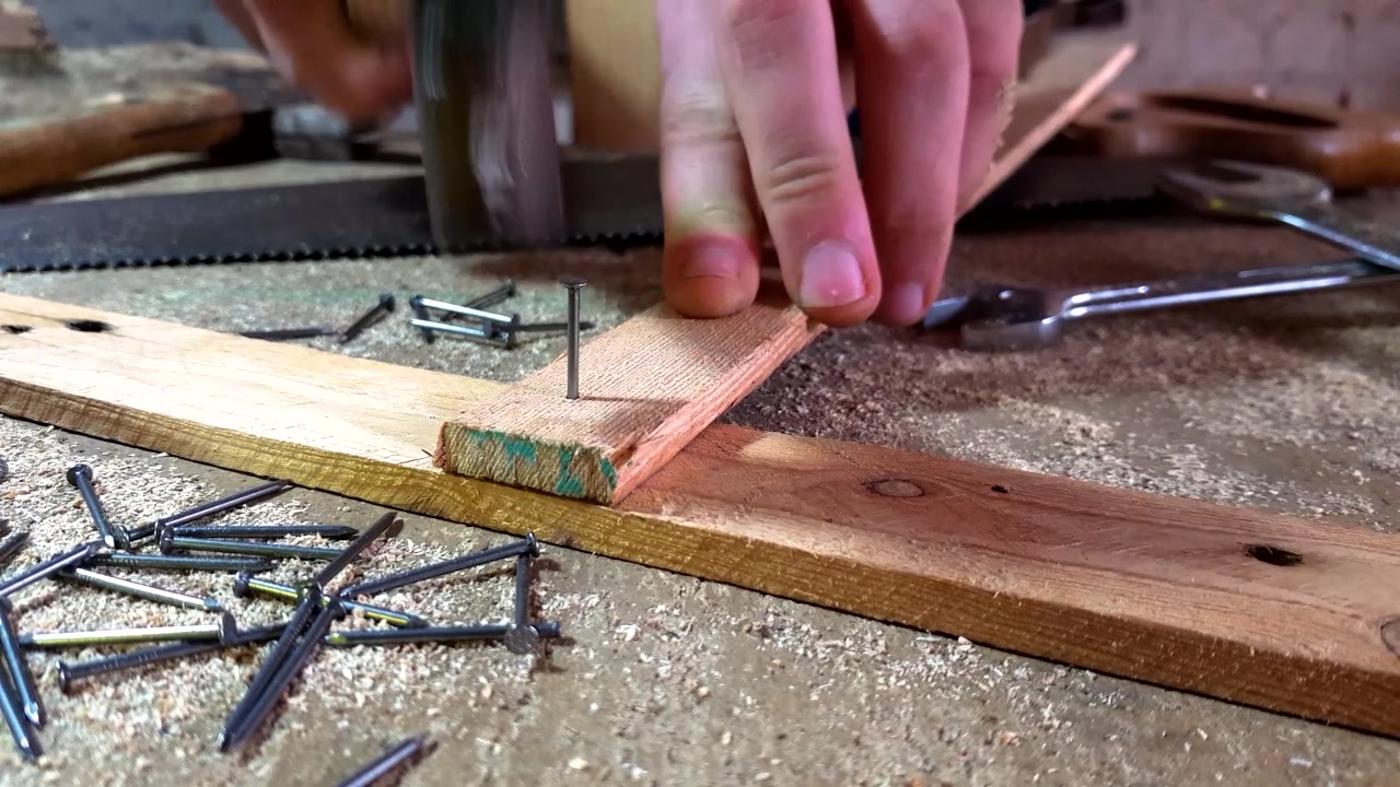 Close-up of hands nailing two pieces of wood together on a work bench