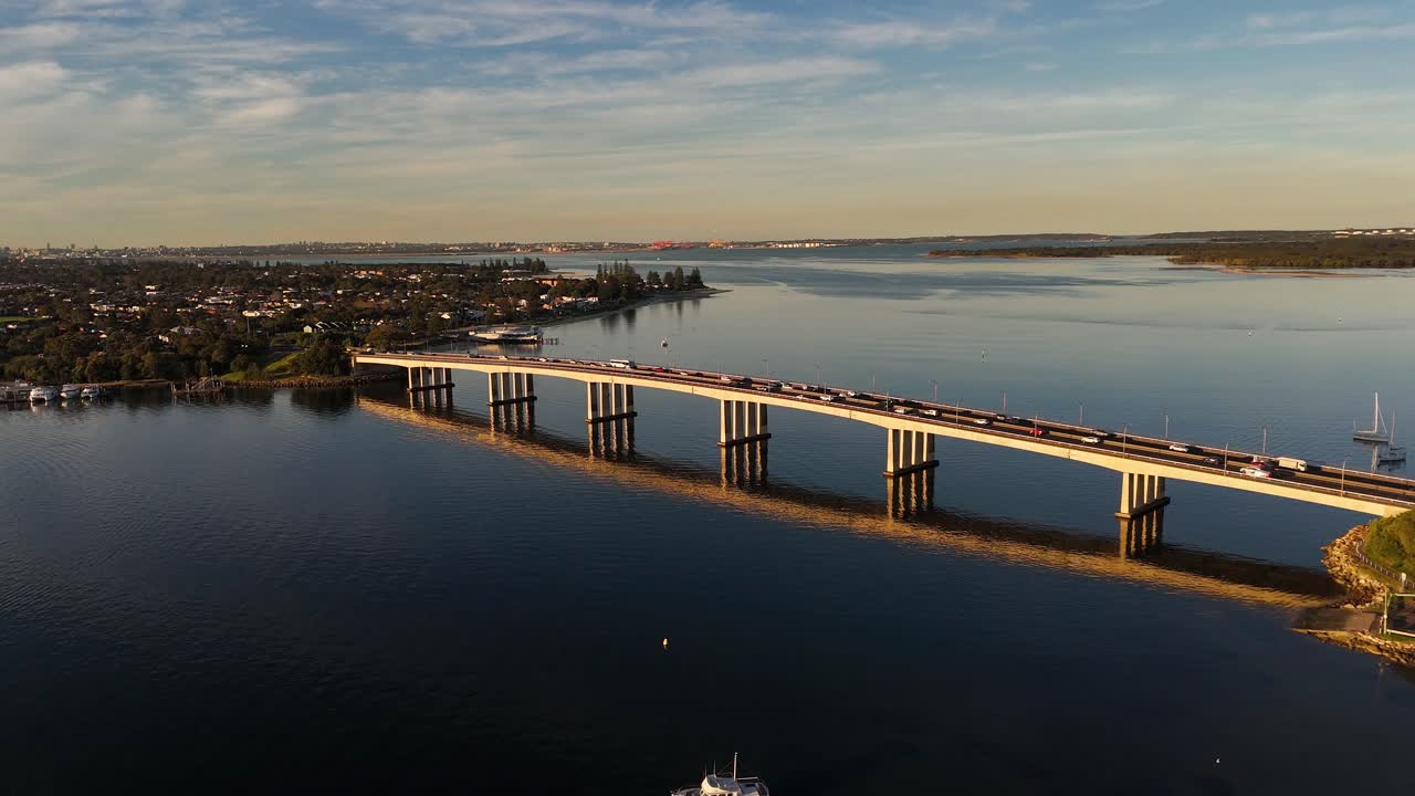 Aerial approach of Captain Cook Bridge over water at golden hour with vibrant tones and calm river, Sydney NSW Australia