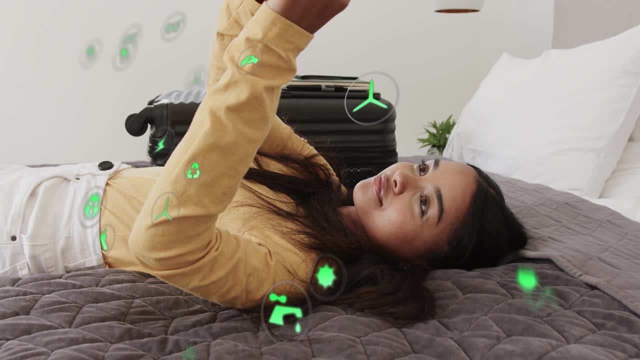 Woman lying on bed tapping phone and generating floating green energy icons while checking usage