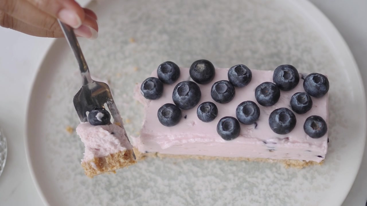 Persona che usa una forchetta per mangiare una fetta di cheesecake ai mirtilli