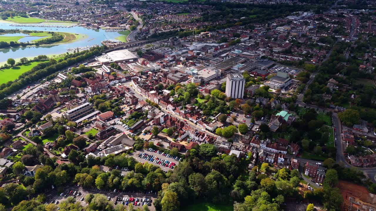 Aerial drone pans left over Fareham town centre with river and trees, capturing roads, cars, and autumn colours glowing warmly in golden sunset light across the scenic English landscape