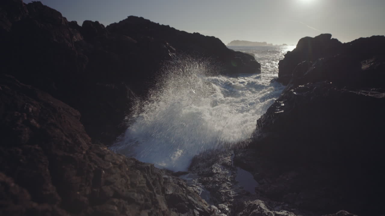 tiro medio inclinado hacia abajo de salpicaduras de olas oceánicas en rocas en un día soleado en ucluelet, isla de vancouver, canadá