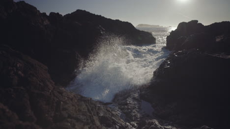 medium tilt down shot of splashing ocean wave on rocks at sunny day in ucluelet, vancouver island, canada