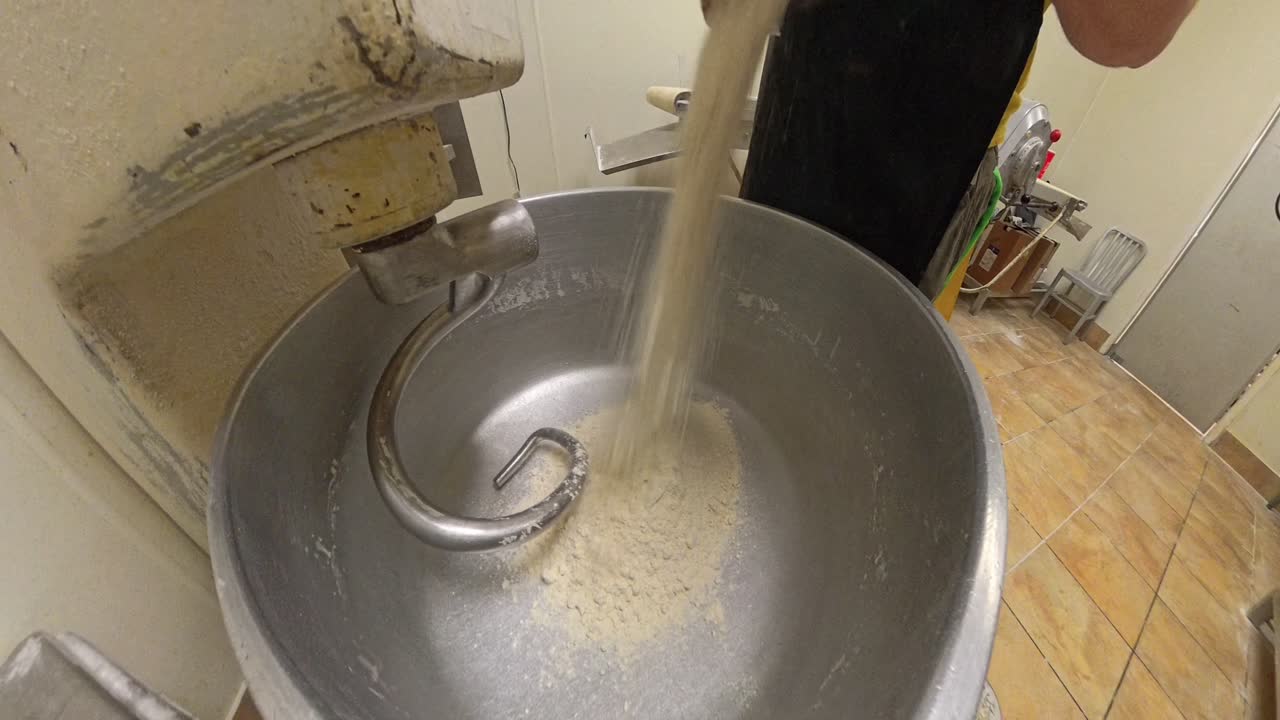Worker pours flour into a giant mixer for a pizza restaurant.