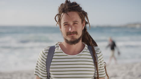 portrait of cute young man smiling happy on beach looking at camera running hand through hair enjoying warm summer vacation