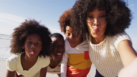 Padres-Afroamericanos-Y-Sus-Hijos-Haciendo-Muecas,-Tomándose-Selfies-Con-Smartphones-En-La-Playa.