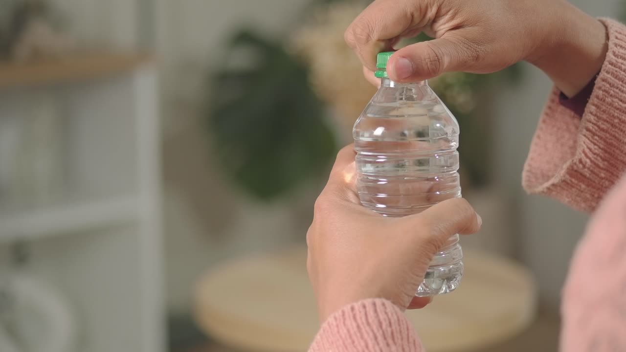 Kädet avaamassa vihreää korkkia pienestä muovisesta vesipullosta