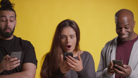 studio shot of group of friends with mobile phones celebrating winning money against yellow background 1