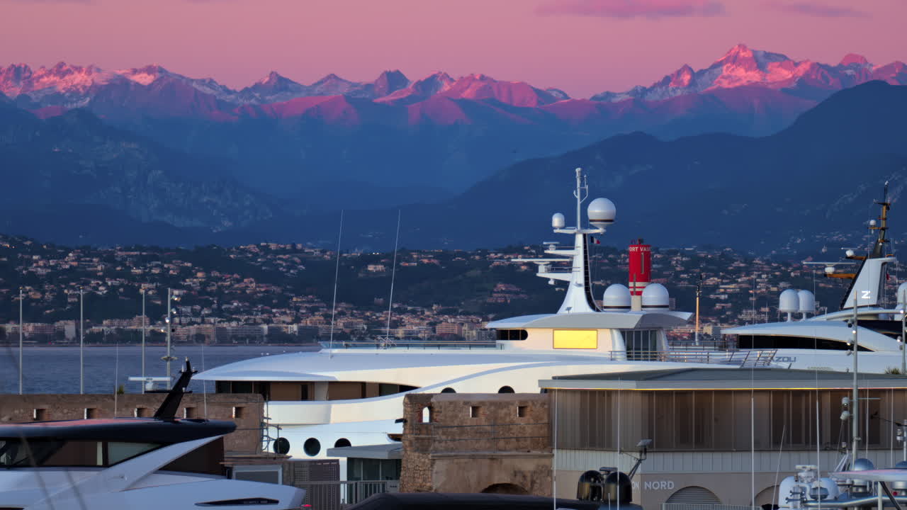 Juan-les-Pins, France - January 25, 2025: Multiple white boats docked in the harbour in Antibes with the mountains on the background at sunset