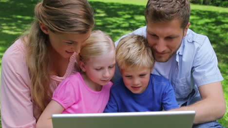 A-family-sitting-together-as-they-use-a-laptop-before-looking-at-the-camera-and-smiling