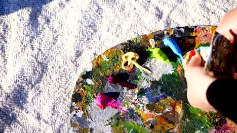 primer plano, manos femeninas con manicura roja brillante. paleta de arte. el artista exprime un poco de pintura azul de un tubo. taller del artista