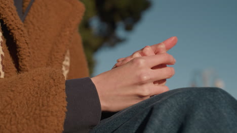 close-up shot of a person's hands rubbing together, suggesting deep contemplation or thought. the person's face is not visible, only blue jeans and a brown coat can be seen, a reflective moment