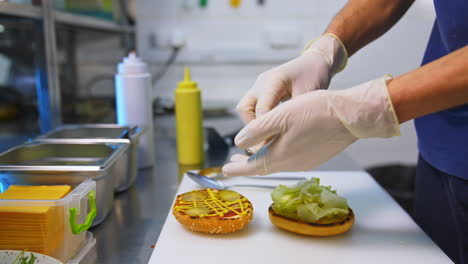 hands in latex gloves put pickles on top of fried bun. making burger on white table. fast food concept video.
