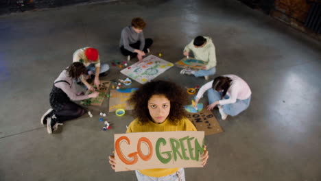 top view of a young environmental activist holding a cardboard with go green" inscription and looking at the camera"