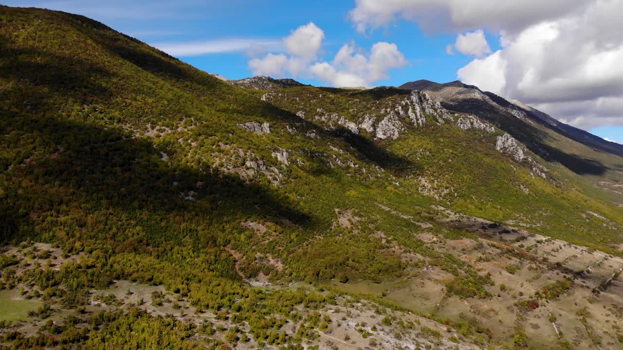 paisaje montañoso paradisíaco con laderas rocosas y bosques bajo nubes blancas en el cielo azul