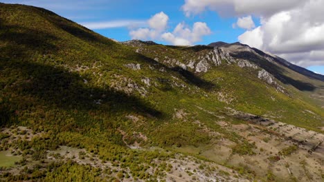 Paradise-mountain-scenery-with-rocky-slopes-and-forests-under-white-clouds-on-blue-sky