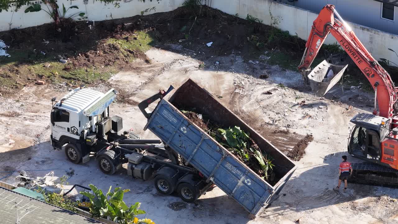 Aerial view of an excavator and dump truck unloading demolition debris at a construction site in Gold Coast, Australia, under bright daylight