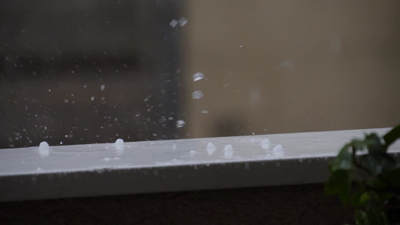 gotas de granizo salpicando y rodando en una barandilla de balcón durante una tormenta en verano, cámara lenta de 180 fps