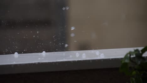 Hail-drops-splashing-and-rolling-on-a-balcony-railing-during-a-storm-at-summer,-180-fps-slow-motion