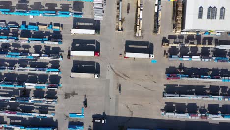 Semi-truck-with-cargo-trailer-is-travelling-on-a-parking-lot-along-a-warehouse-of-a-logistics-park