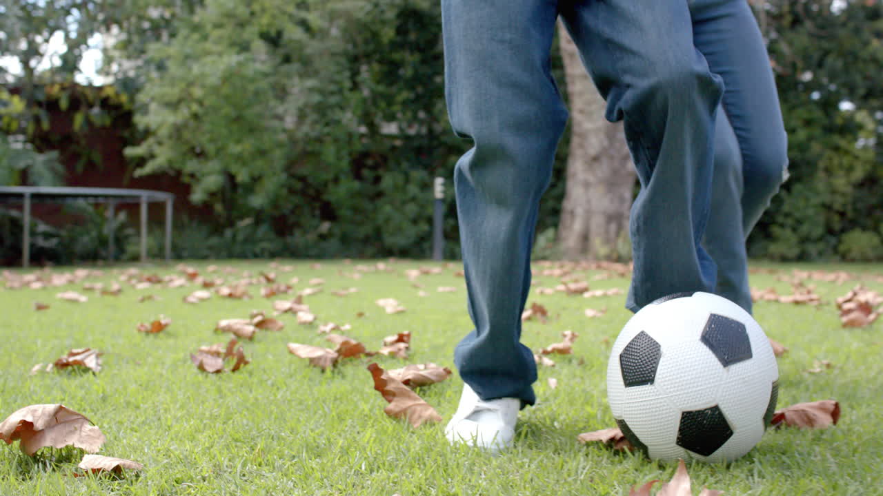 Midsection of african american mother and son playing football in garden, in slow motion