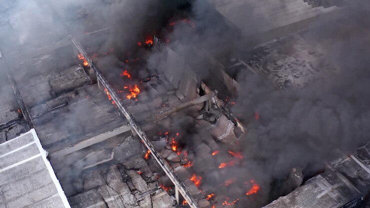 Aerial view of a blazing building fire, black smoke rising from a burning structure - approaching, drone shot